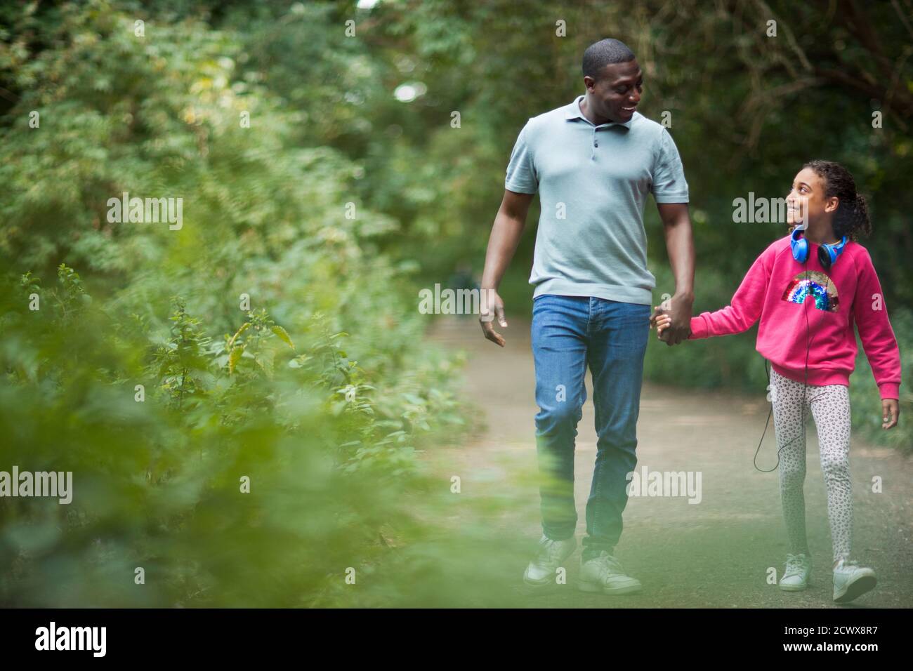 Father and daughter holding hands on path in woods Stock Photo