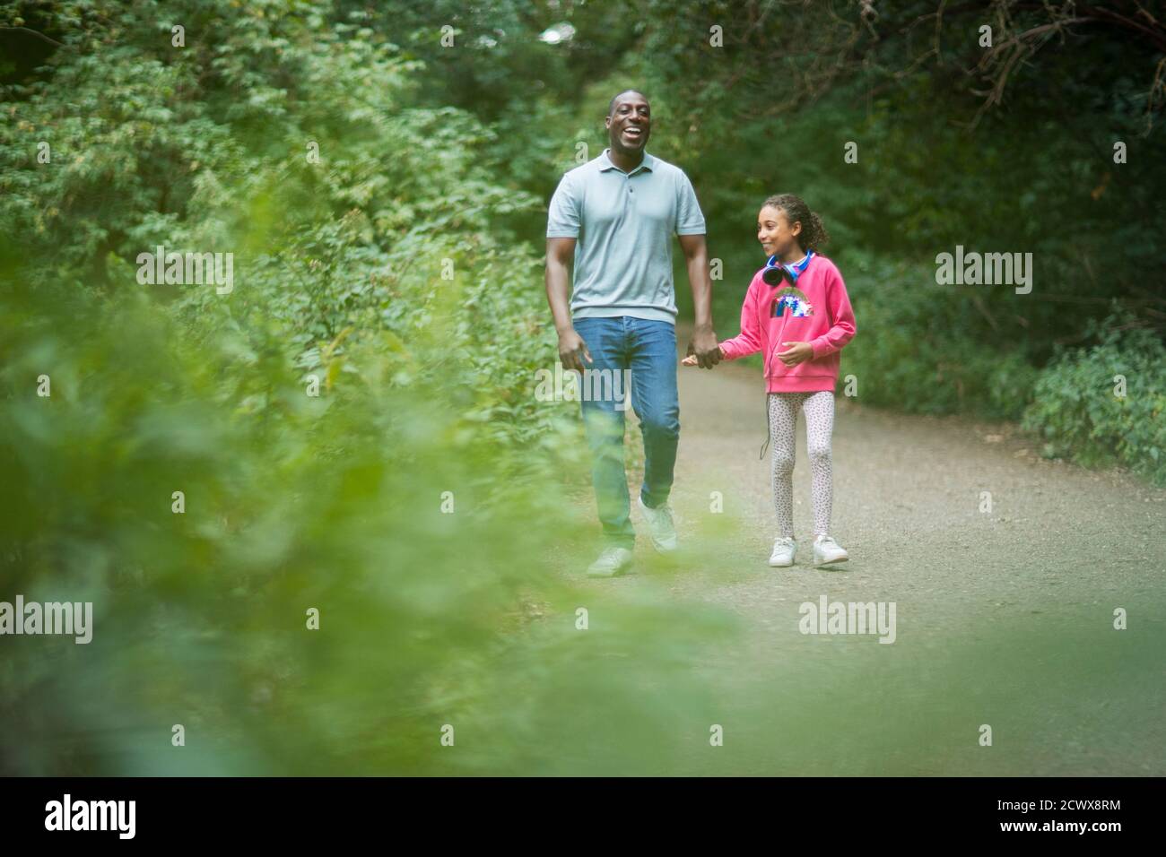Happy father and daughter holding hands on path in woods Stock Photo