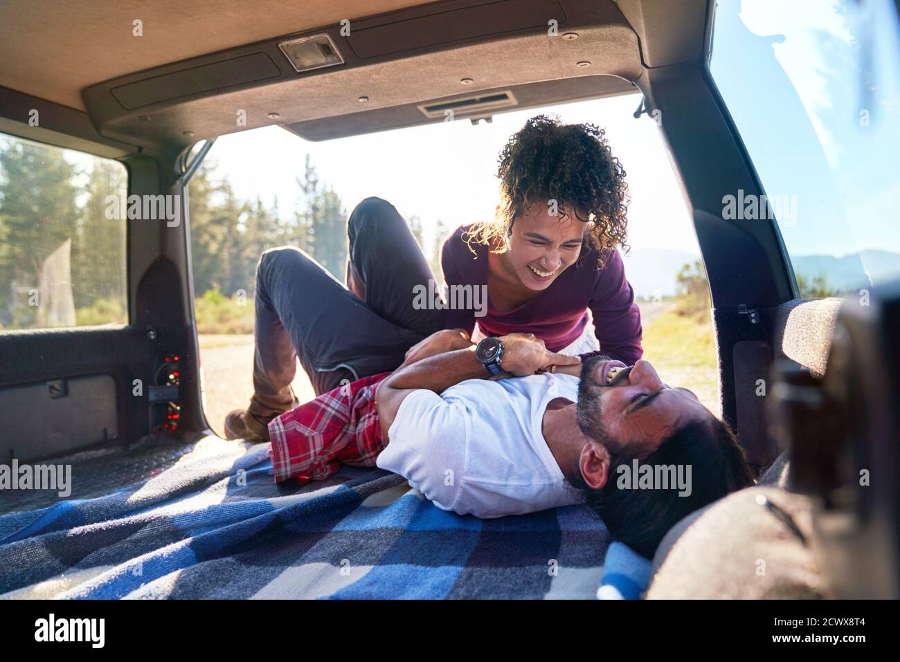 Happy playful young couple laughing on road trip at back of car Stock Photo