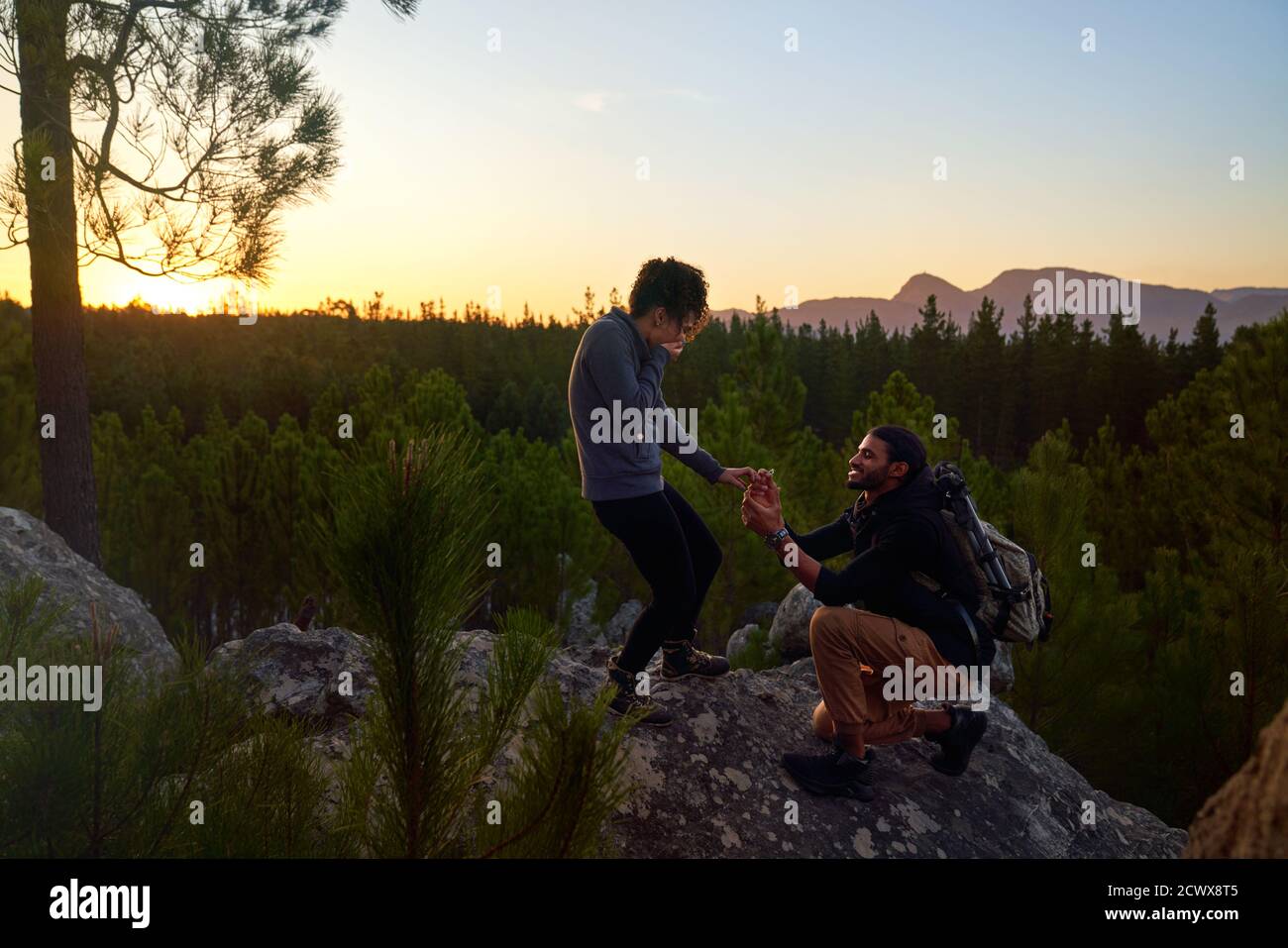 Young man with engagement ring proposing to woman on rock at sunset Stock Photo