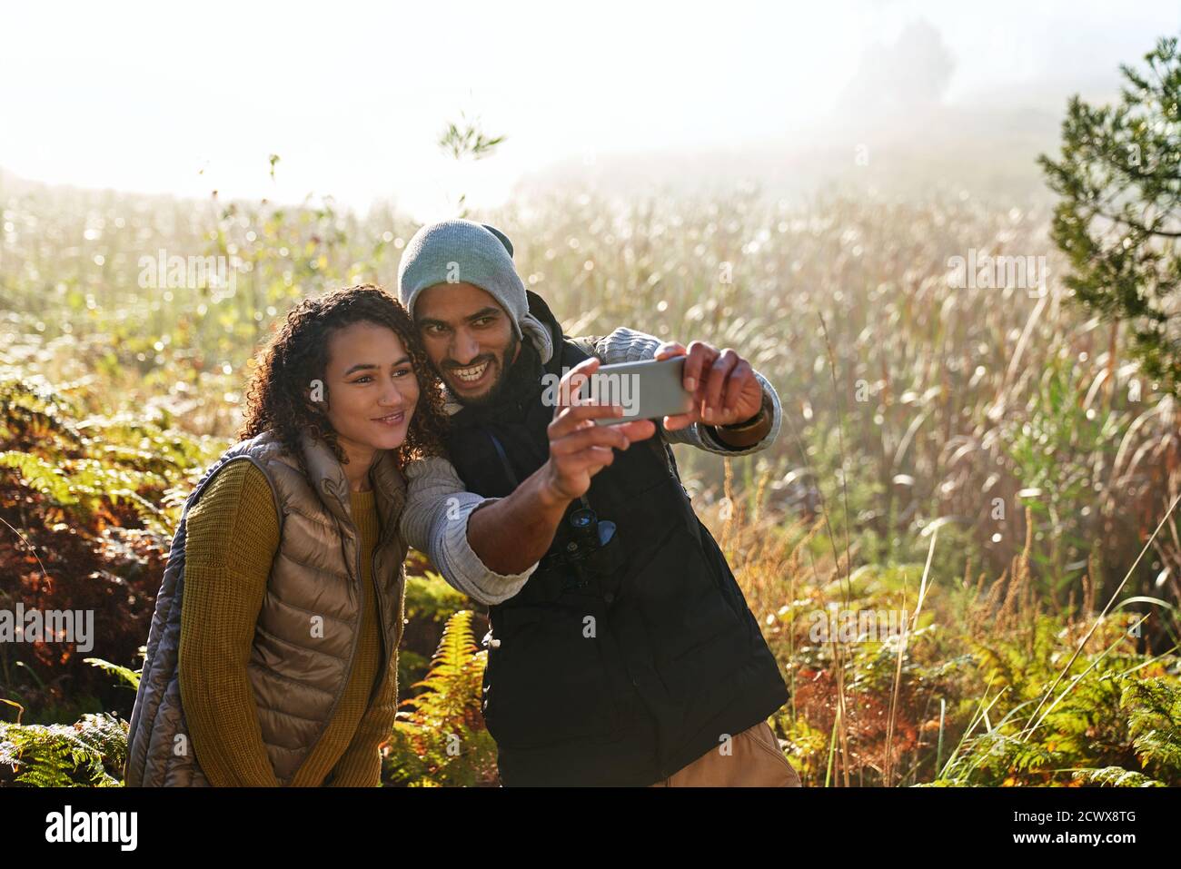 Happy young couple with camera phone taking selfie in sunny tall grass Stock Photo