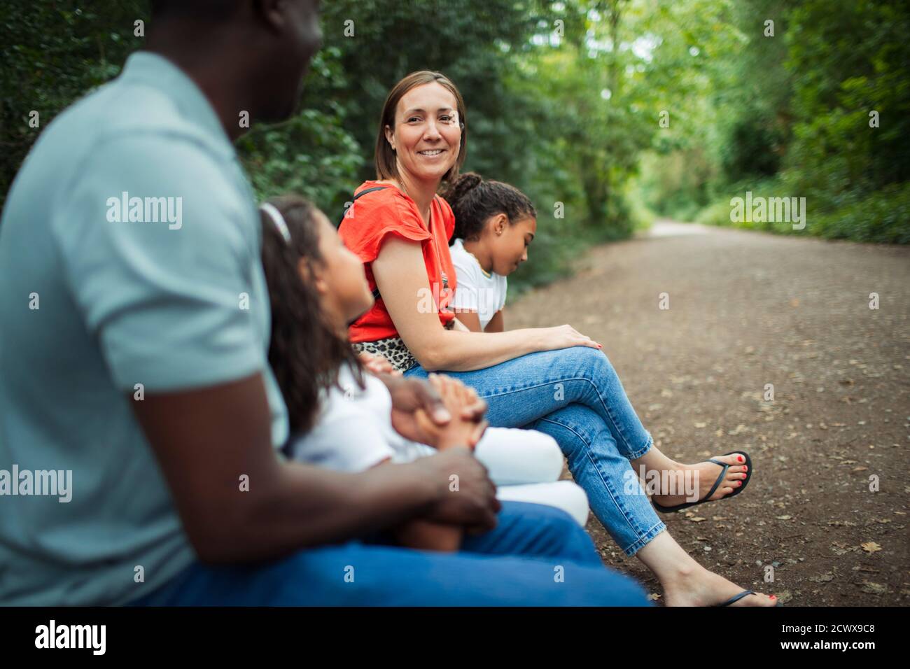 Happy family sitting on bench on path in park Stock Photo