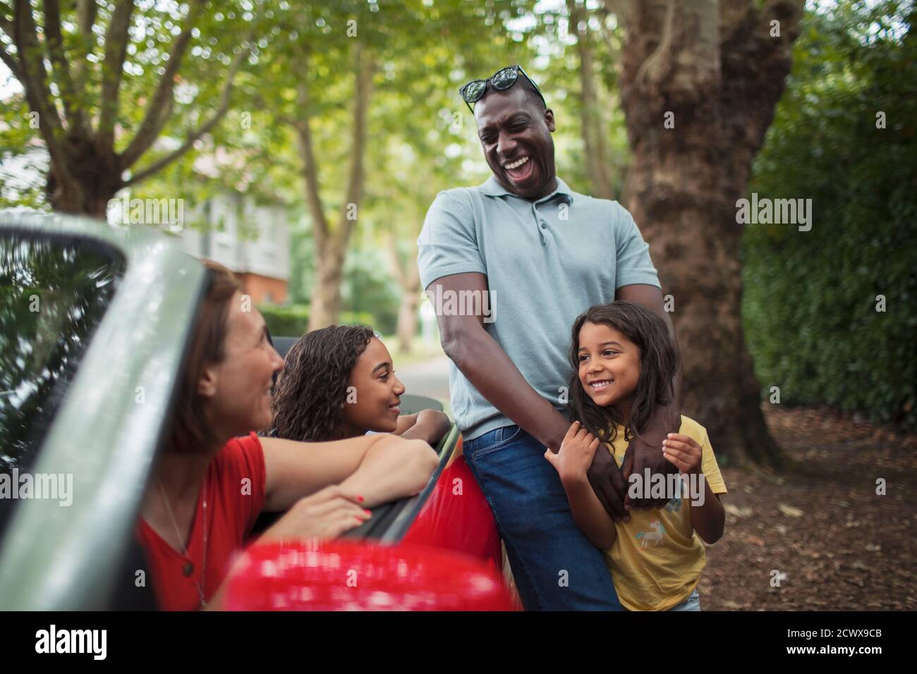 Happy family laughing at convertible in driveway Stock Photo