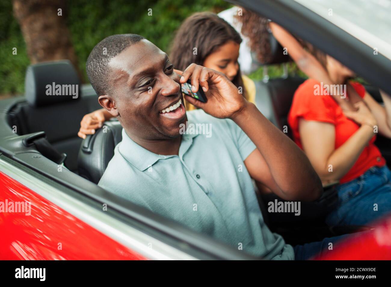 Happy man talking on smart phone in convertible with family Stock Photo