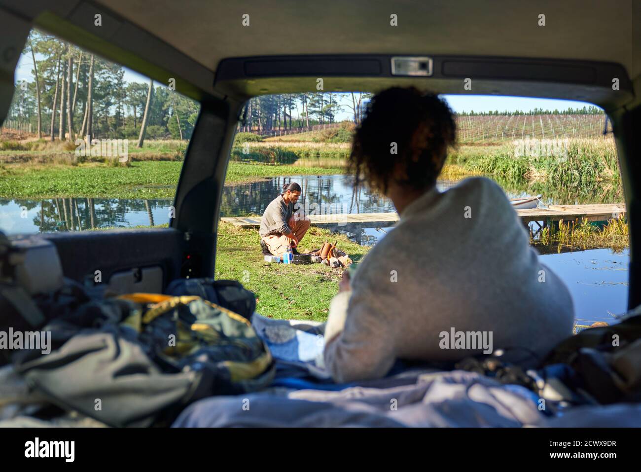 Young woman in car watching boyfriend prepare campfire Stock Photo
