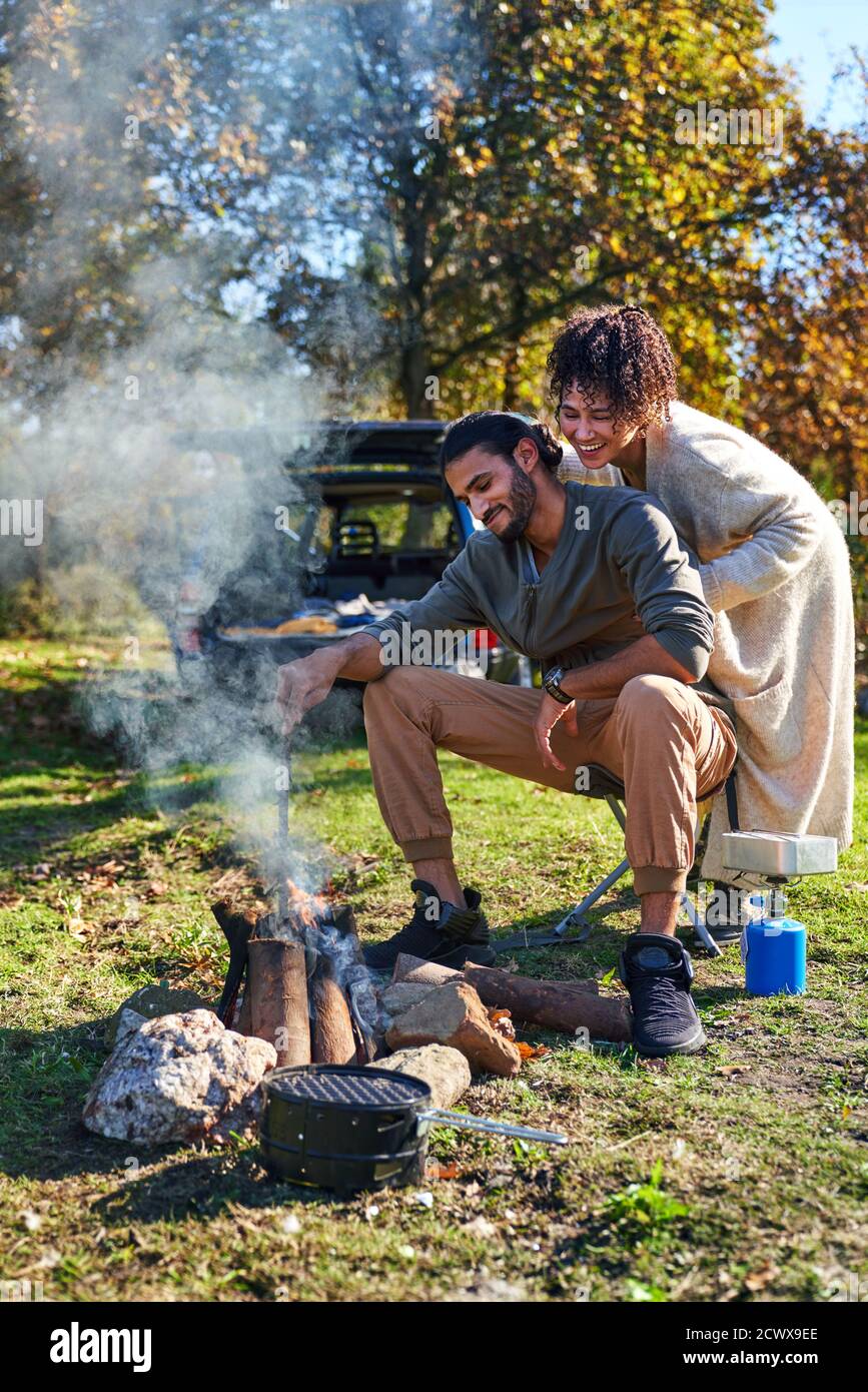 Happy young couple enjoying campfire in sunny autumn field Stock Photo