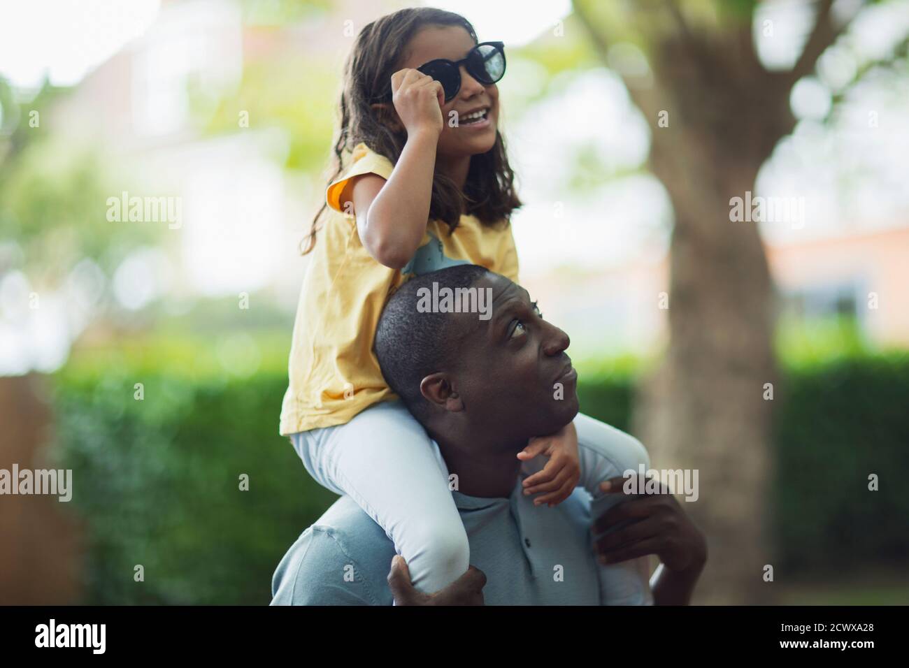 Father carrying daughter with sunglasses on shoulders Stock Photo