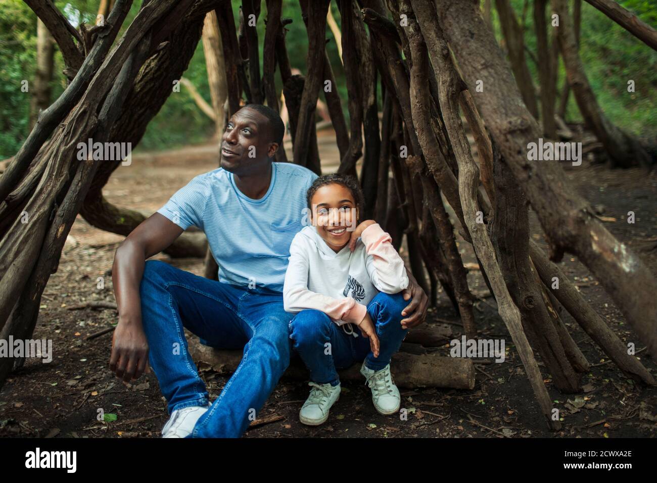 Happy father and daughter relaxing inside tree branch teepee in woods Stock Photo