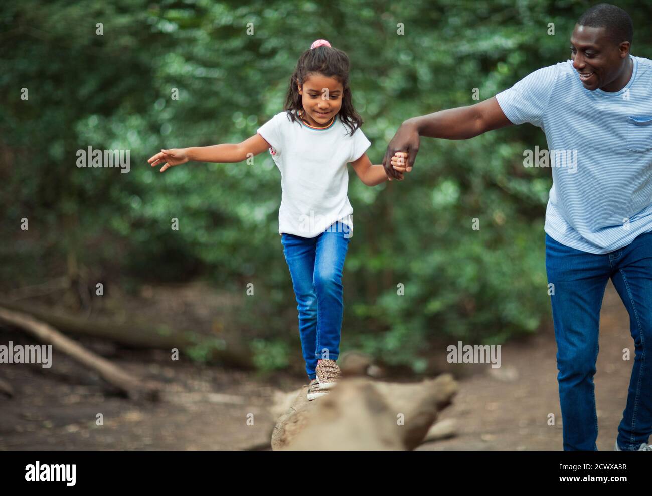 Father helping daughter balance on fallen log in woods Stock Photo