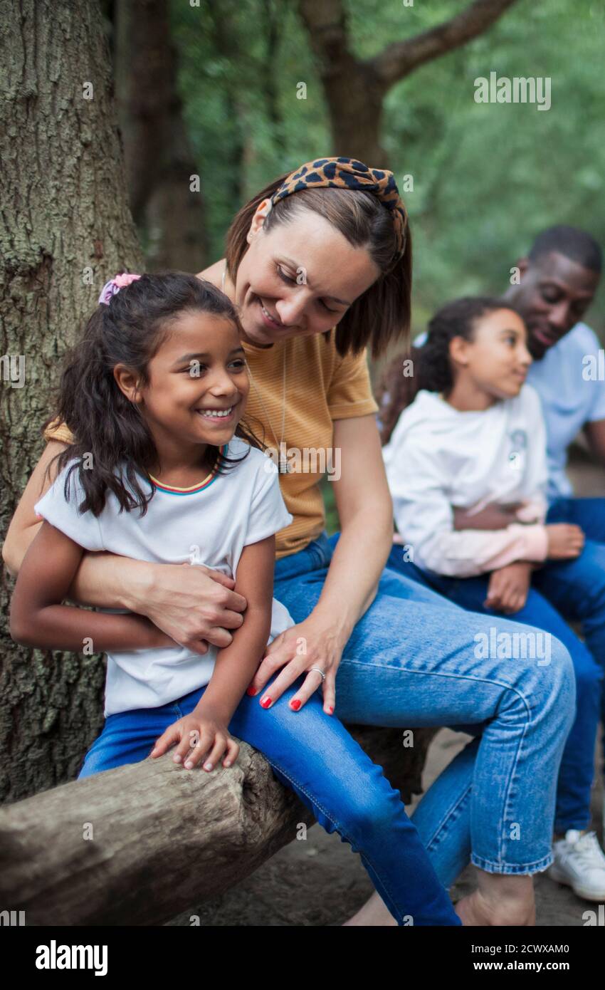 Happy mother and daughter hugging on fallen log in woods Stock Photo
