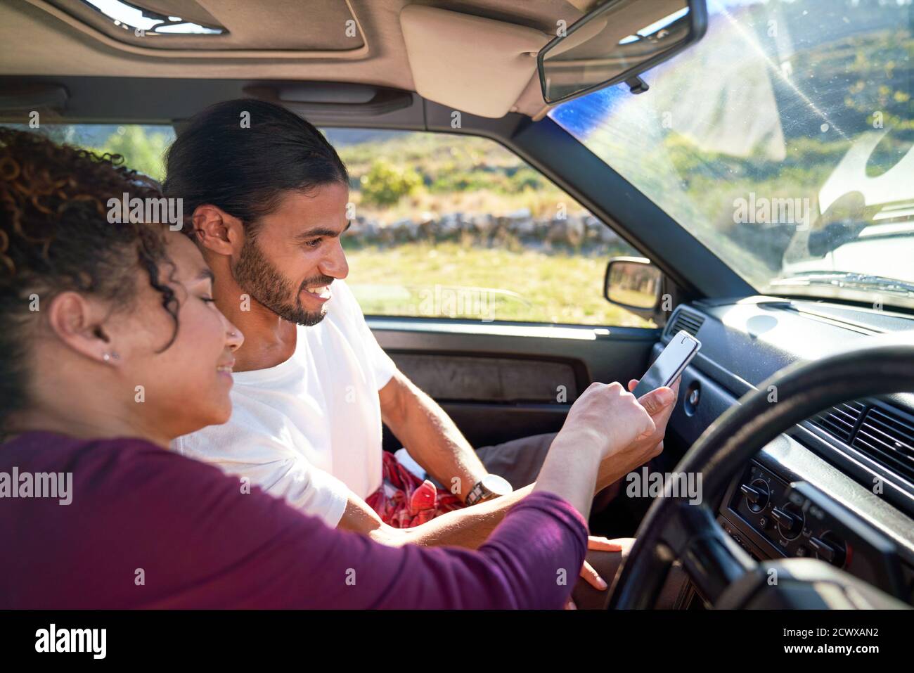 Young couple using smart phone on road trip in sunny car Stock Photo