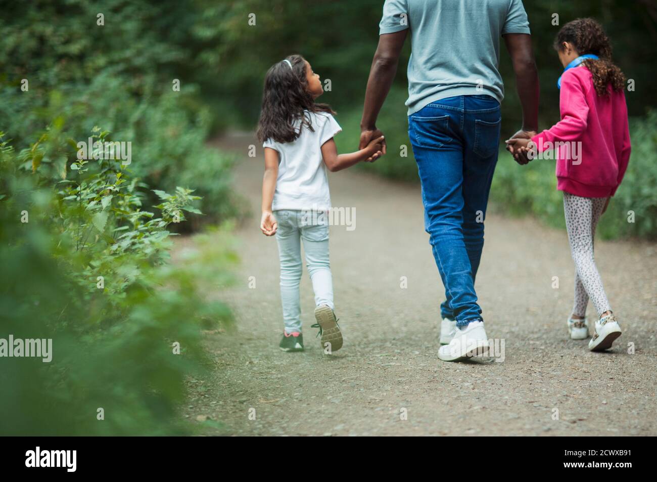 Father and daughters holding hands walking on path in park Stock Photo