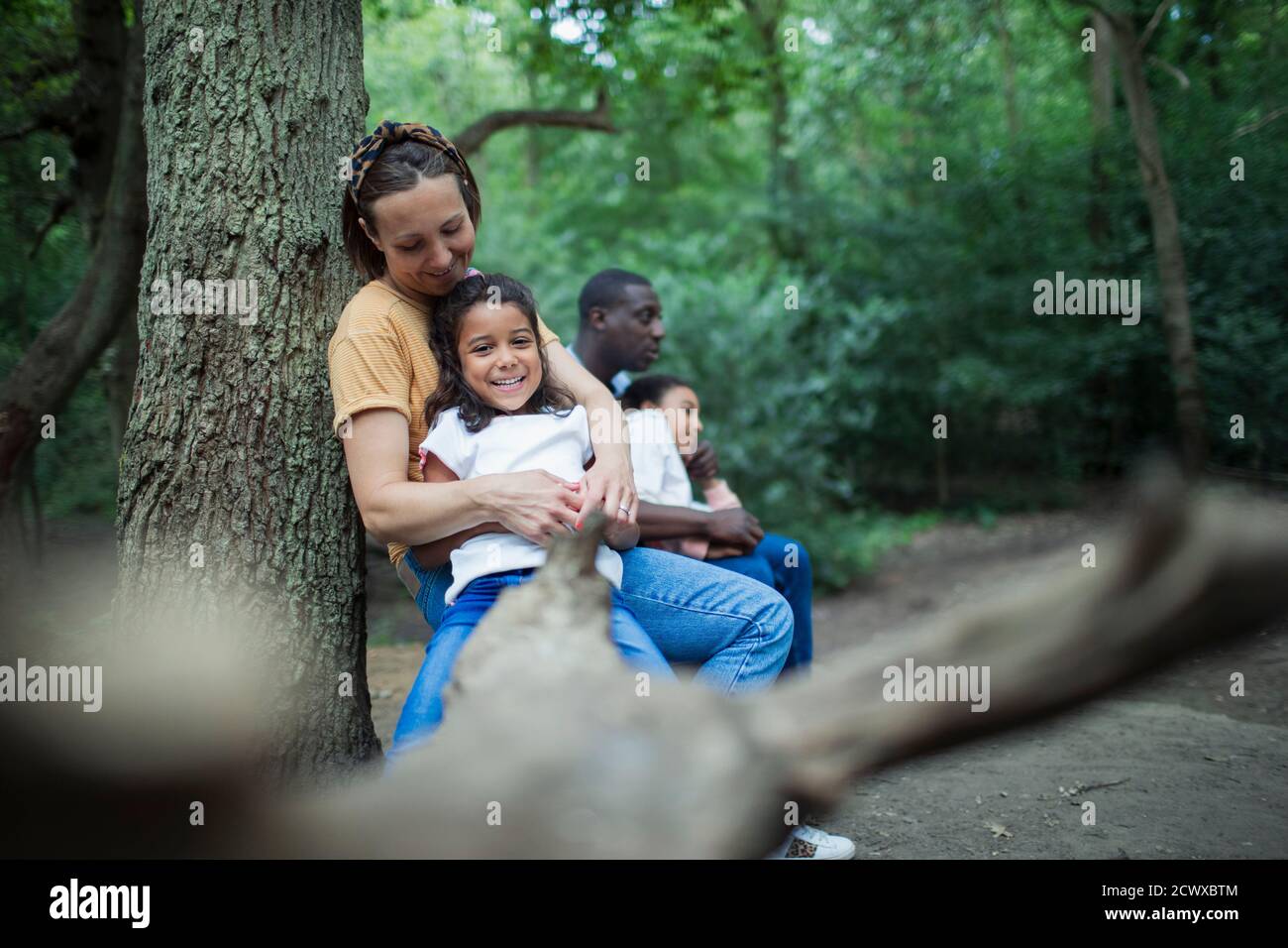 Happy family relaxing on fallen log on hike in woods Stock Photo