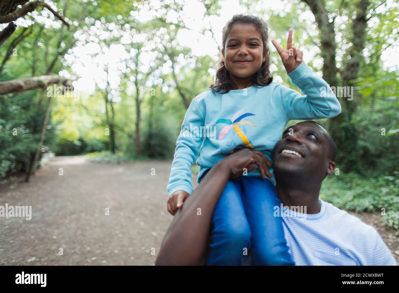 Portrait father carrying daughter gesturing peace sign in woods Stock Photo