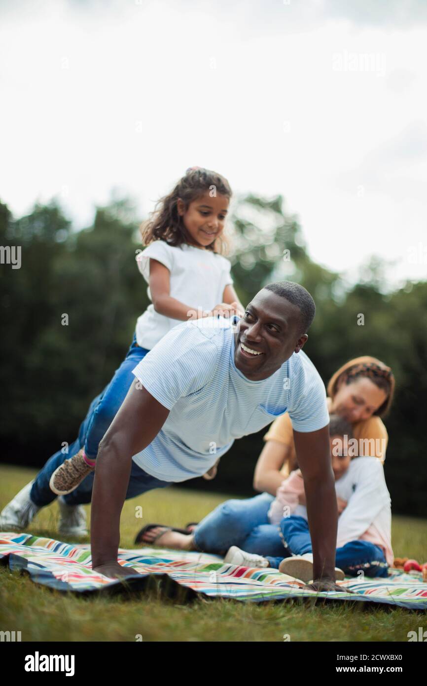 Playful father doing push ups with daughter on back in park Stock Photo