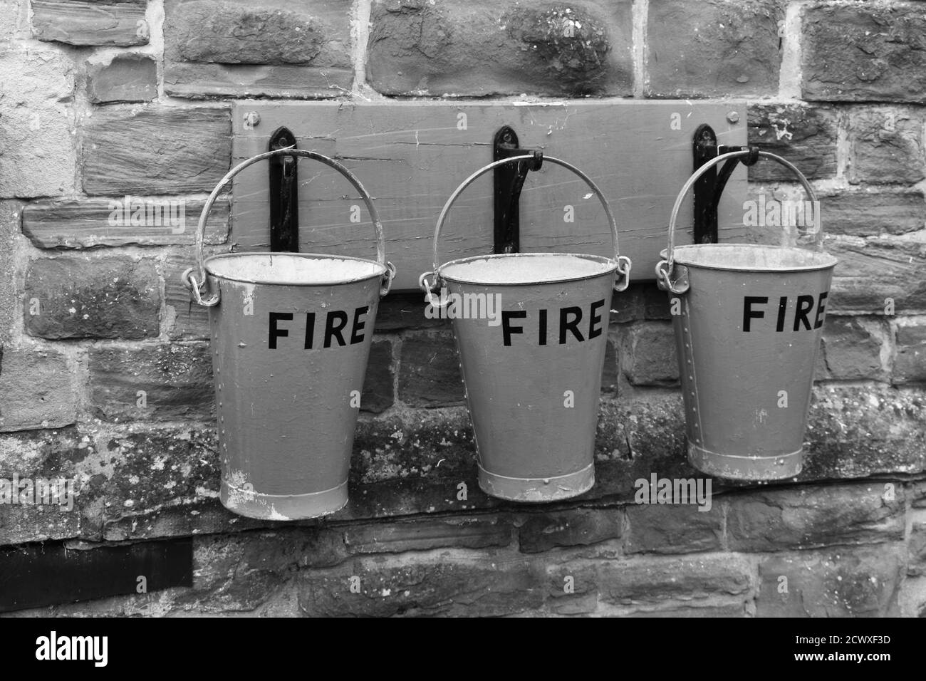 close up of 3 red Fire buckets hanging from hooks on a stone wall outside Stock Photo