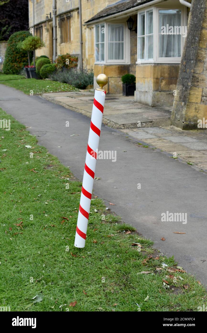 close up of red and white barbers pole outside stuck in grass alongside pavement in autumn sun Stock Photo