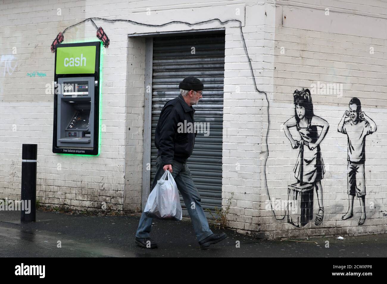 A man walks past art work by graffiti artist The Rebel Bear which has recently appeared showing two children about to detonate explosives at a cashline at a shopping centre in Cambuslang. Over recent months the artist has drawn several coronavirus related drawings in Glasgow. Stock Photo