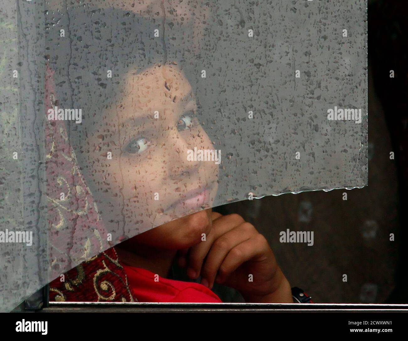 A boy looks through the broken window of a bus covered with rain drops as  it rains in Srinagar August 4, 2012. A moderate rainfall in Srinagar since  Friday evening brought down