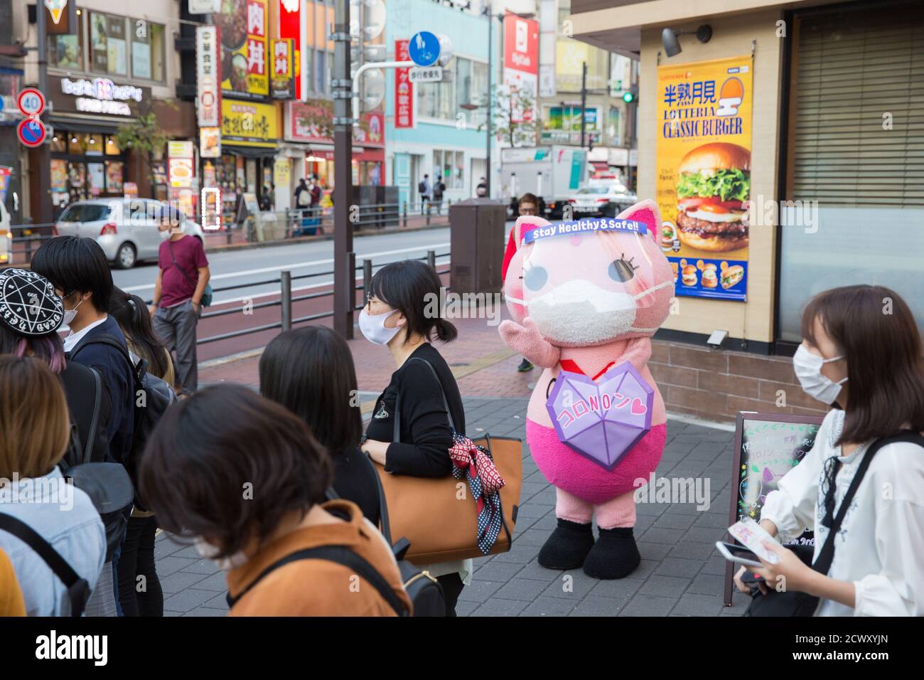 Koronon, a Japanese anti-coronavirus cat mascot waves at pedestrians wearing masks in Ikebukuro, Tokyo.Koronon, a Japanese anti-coronavirus cat mascot who hands out disposable face masks and raises awareness about the coronavirus (Covid-19) waves at pedestrians in Ikebukuro, Tokyo. Koronon can also be booked to visit schools and companies to share its message about hygiene and other measures to fight Covid-19. Stock Photo