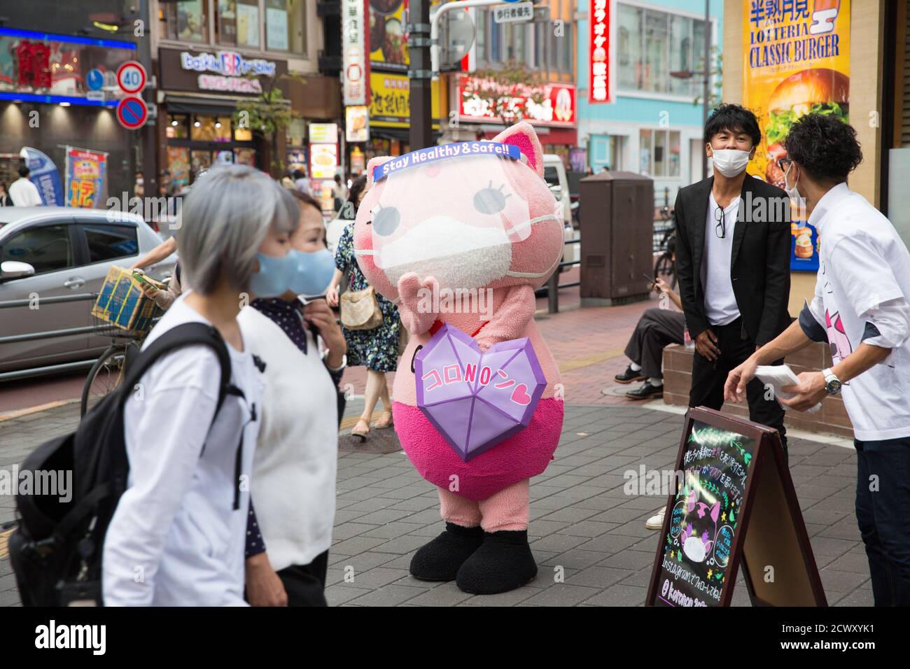 Koronon, a Japanese anti-coronavirus cat mascot waves at pedestrians wearing facemasks.Koronon, a Japanese anti-coronavirus cat mascot who hands out disposable face masks and raises awareness about the coronavirus (Covid-19) waves at pedestrians in Ikebukuro, Tokyo. Koronon can also be booked to visit schools and companies to share its message about hygiene and other measures to fight Covid-19. Stock Photo
