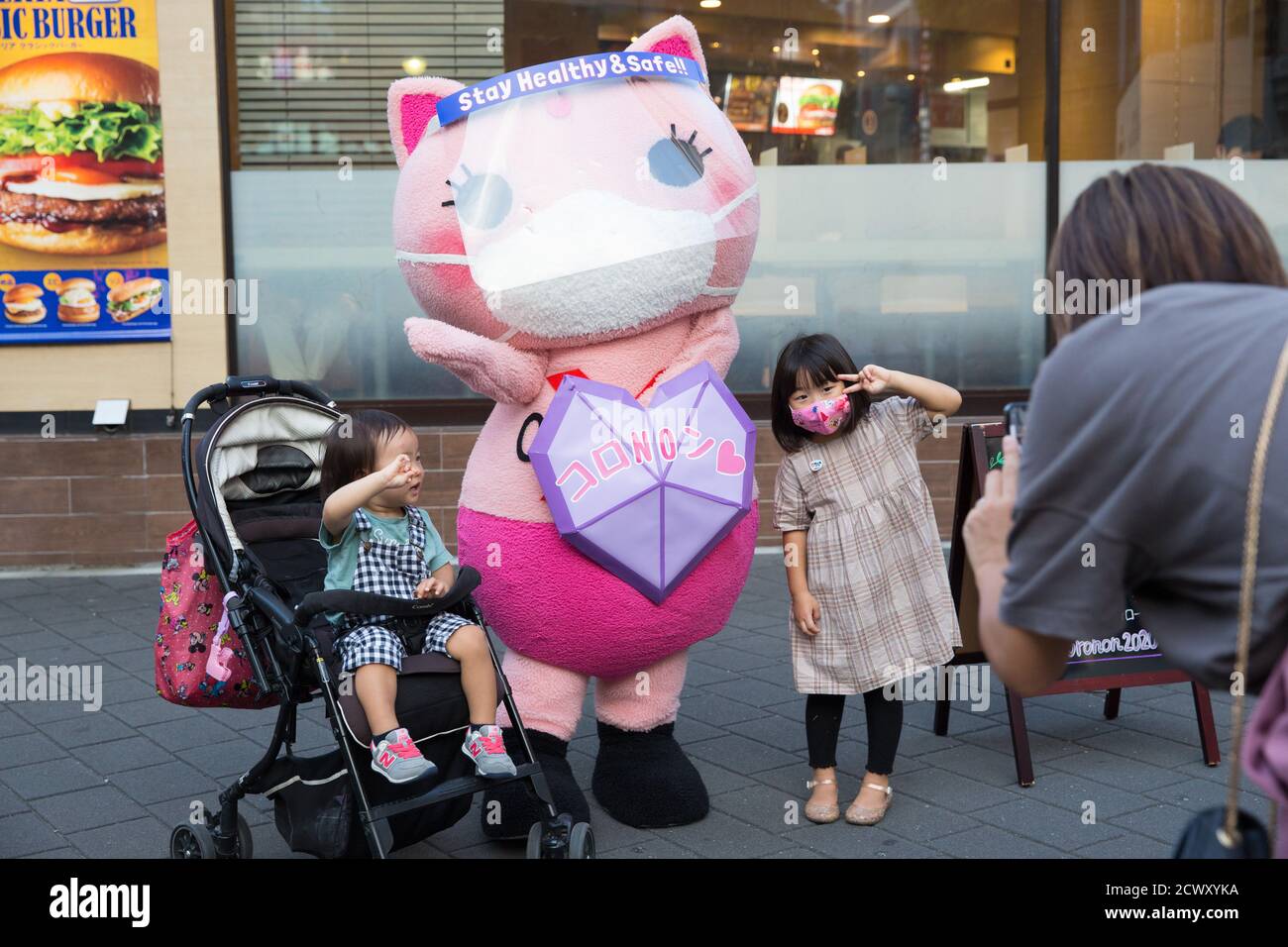 Koronon, a Japanese anti-coronavirus cat mascot poses with children for a photo in Ikebukuro, Tokyo.Koronon, a Japanese anti-coronavirus cat mascot who hands out disposable face masks and raises awareness about the coronavirus (Covid-19) waves at pedestrians in Ikebukuro, Tokyo. Koronon can also be booked to visit schools and companies to share its message about hygiene and other measures to fight Covid-19. Stock Photo