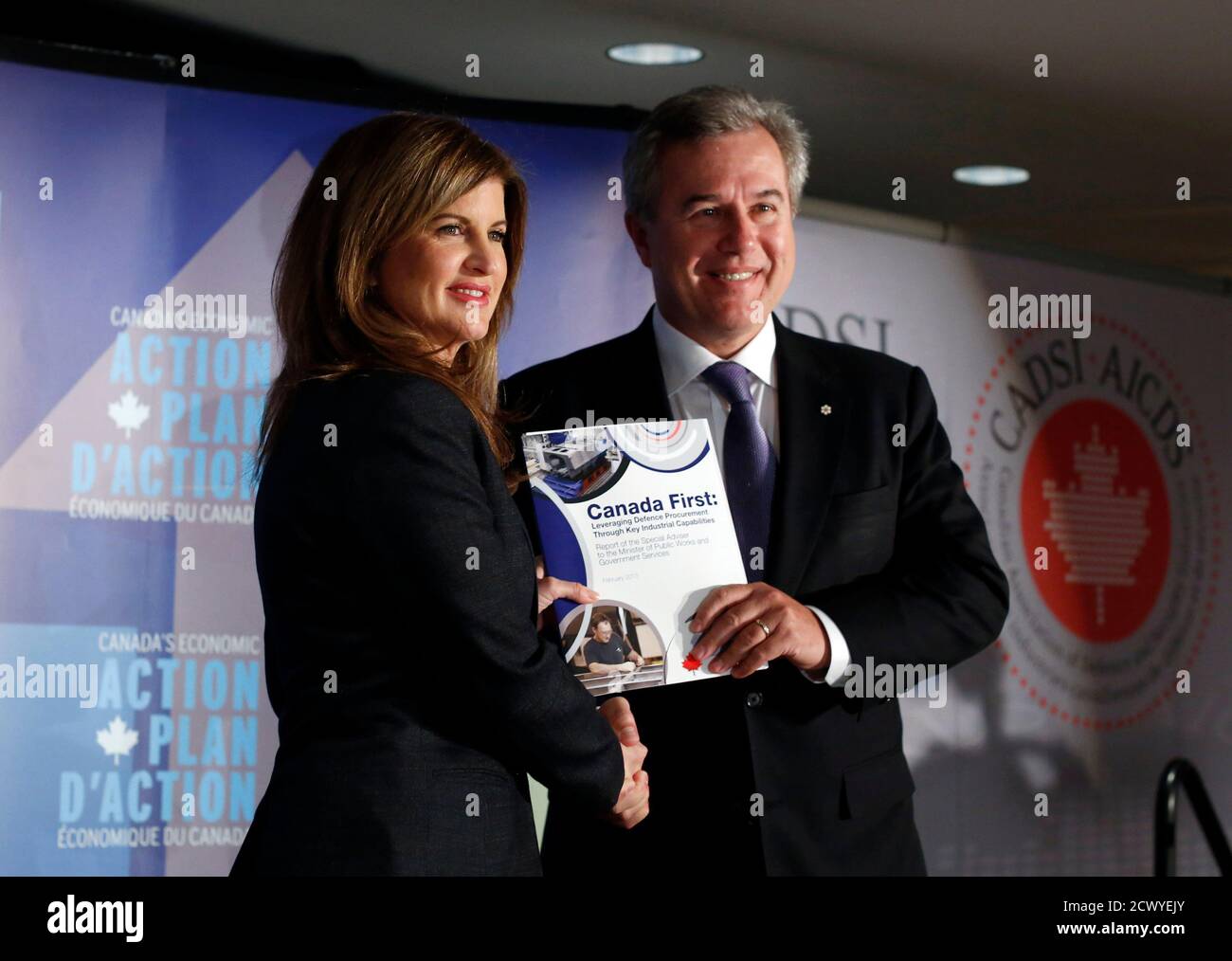 OpenText Corporation executive chairman Tom Jenkins (R) holds his report on  military procurement with Canada's Public Works Minister Rona Ambrose at  the start of a news conference in Ottawa February 12, 2013.