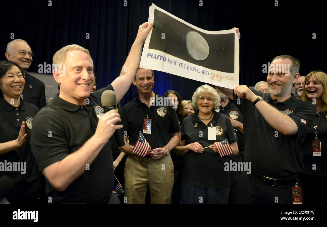 NASA Principal Investigator for New Horizons mission Alan Stern (L) and Co-Investigator Will Grundy (R) hold up an enlarged, out-dated U.S. postage stamp with the words 'PLUTO NOT YET EXPLORED', during the celebration of the spacecraft New Horizons flyby of Pluto, at NASA's Johns Hopkins Applied Physics Laboratory in Laurel, Maryland, July 14, 2015. Also attending are APL Director Ralph Semmel (center,L) and Annette Tombaugh, daughter of Pluto's discoverer Clyde Tombaugh (center,R). The flyby, which culminated after almost ten years of flight and over three billion miles, will allow New Horizo Stock Photo