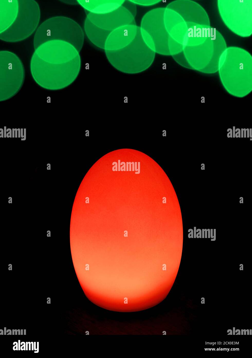 Shining Vibrant Red Egg Shaped Table Lamp with Vivid Green Bokeh Light on Dark Background Stock Photo