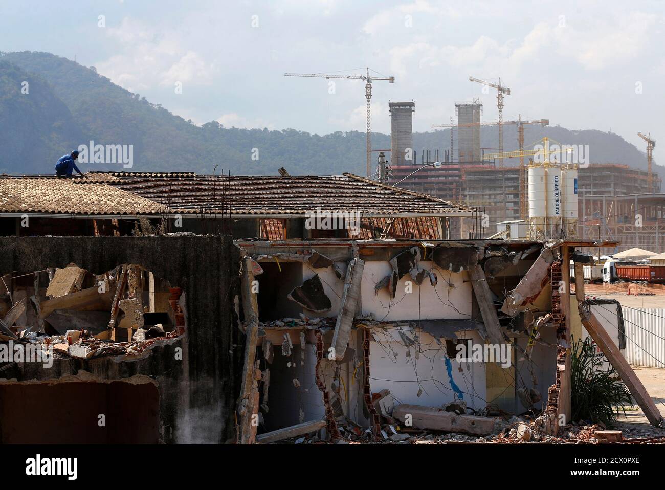 A Worker Works On The Demolition Of A House With Cranes And Construction Work For The Rio 16 Olympic Park Seen In The Background At The Vila Autodromo Favela In Rio De