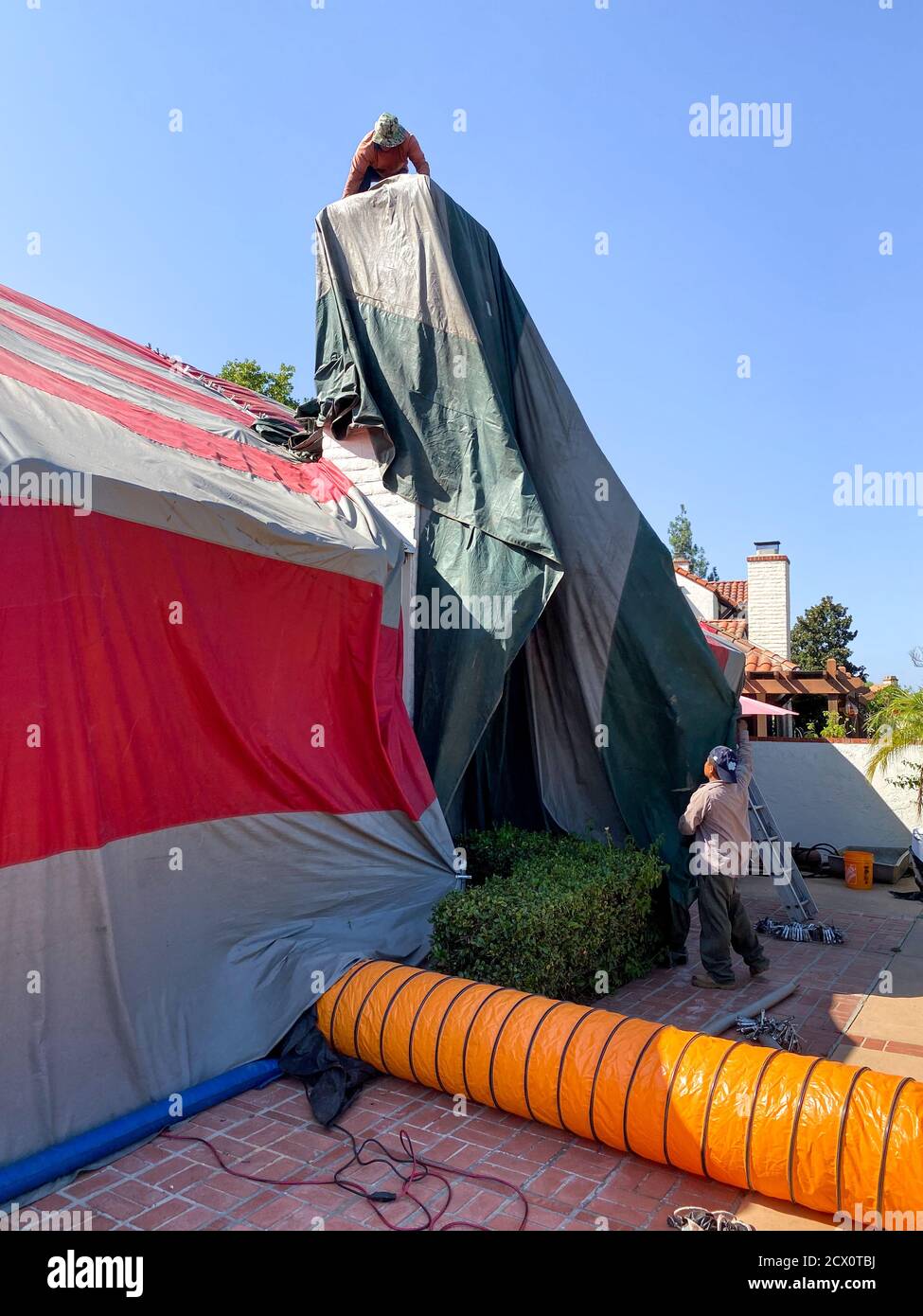 Worker installing a tent on a residential villa for termite fumigation