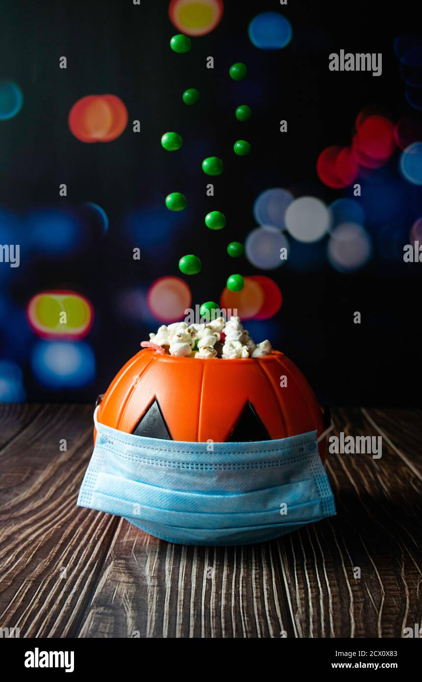 Vertical shot of a Halloween pumpkin with green jelly beans falling on it. The pumpkin has a hygienic mask to prevent Covid-19 Stock Photo