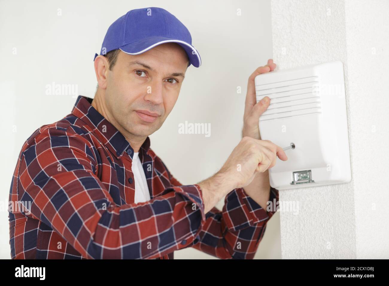 male electrician installing security system door sensor on wall Stock