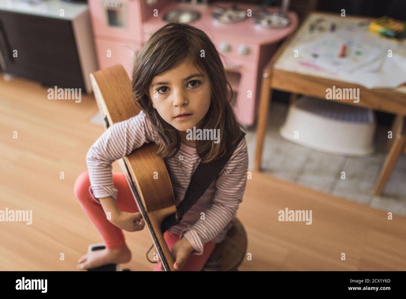 Young girl with deep brown eyes on stool holding small guitar Stock Photo -  Alamy, image size:1300x957