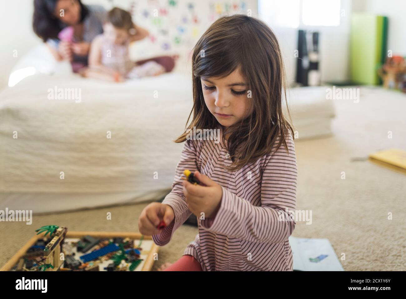 Young old girl wearing striped shirt on floor playing with Legos Stock Photo