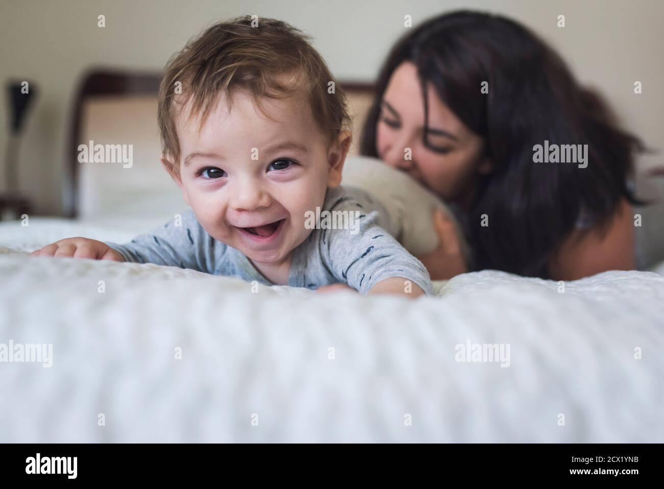 Laughing year old baby on stomach on bed with playful mid-30's mother Stock Photo