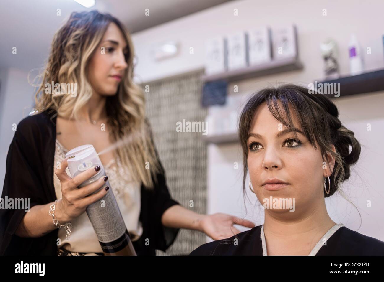 Young female hairdresser applying spray on client's hair. Female hairdresser works on woman hair
