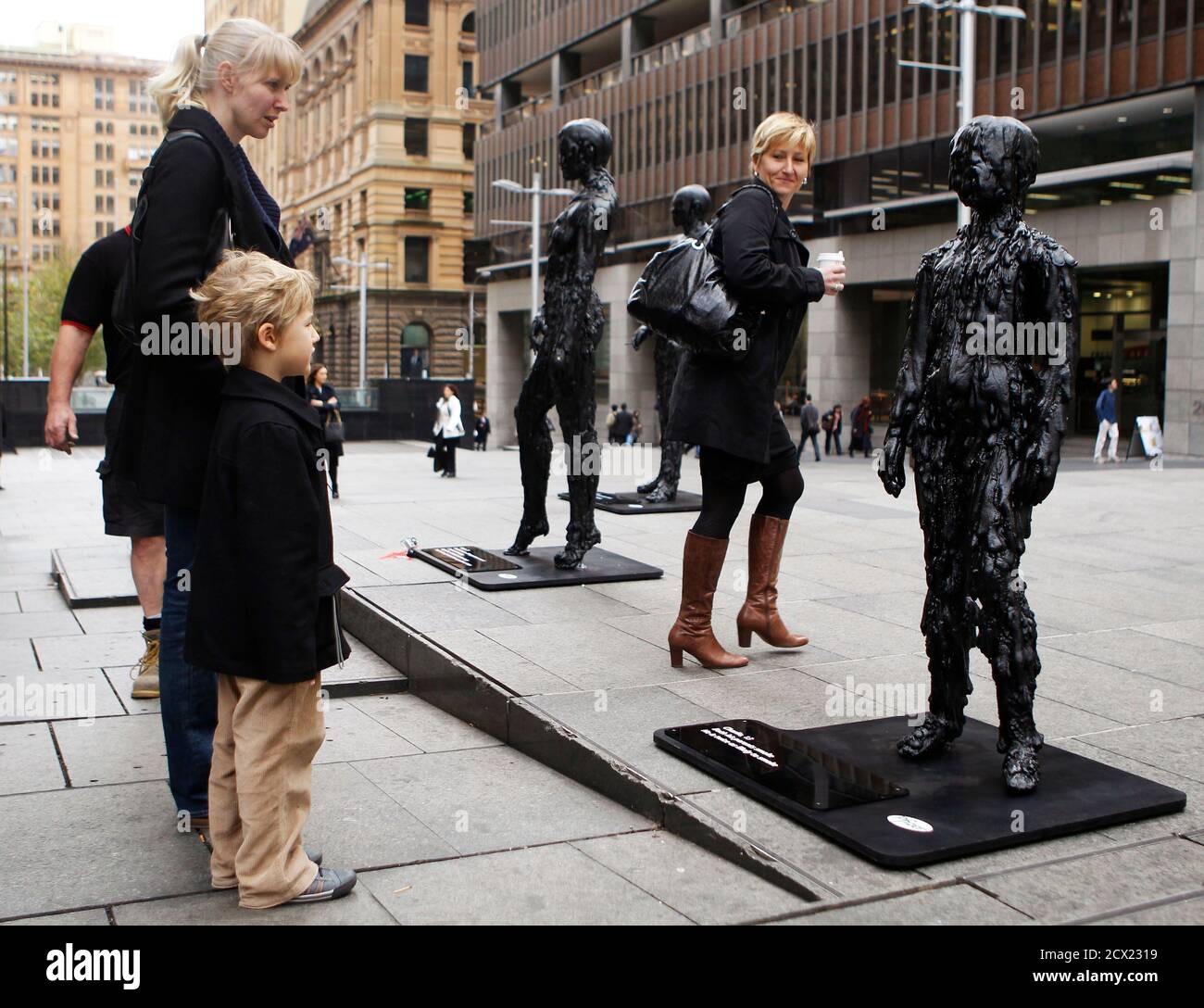 A boy looks at a statue which looks like a child covered in tar at Martin  Place in Central Sydney June 30, 2011. "Tarmy", 20 statues of people  covered in tar, are