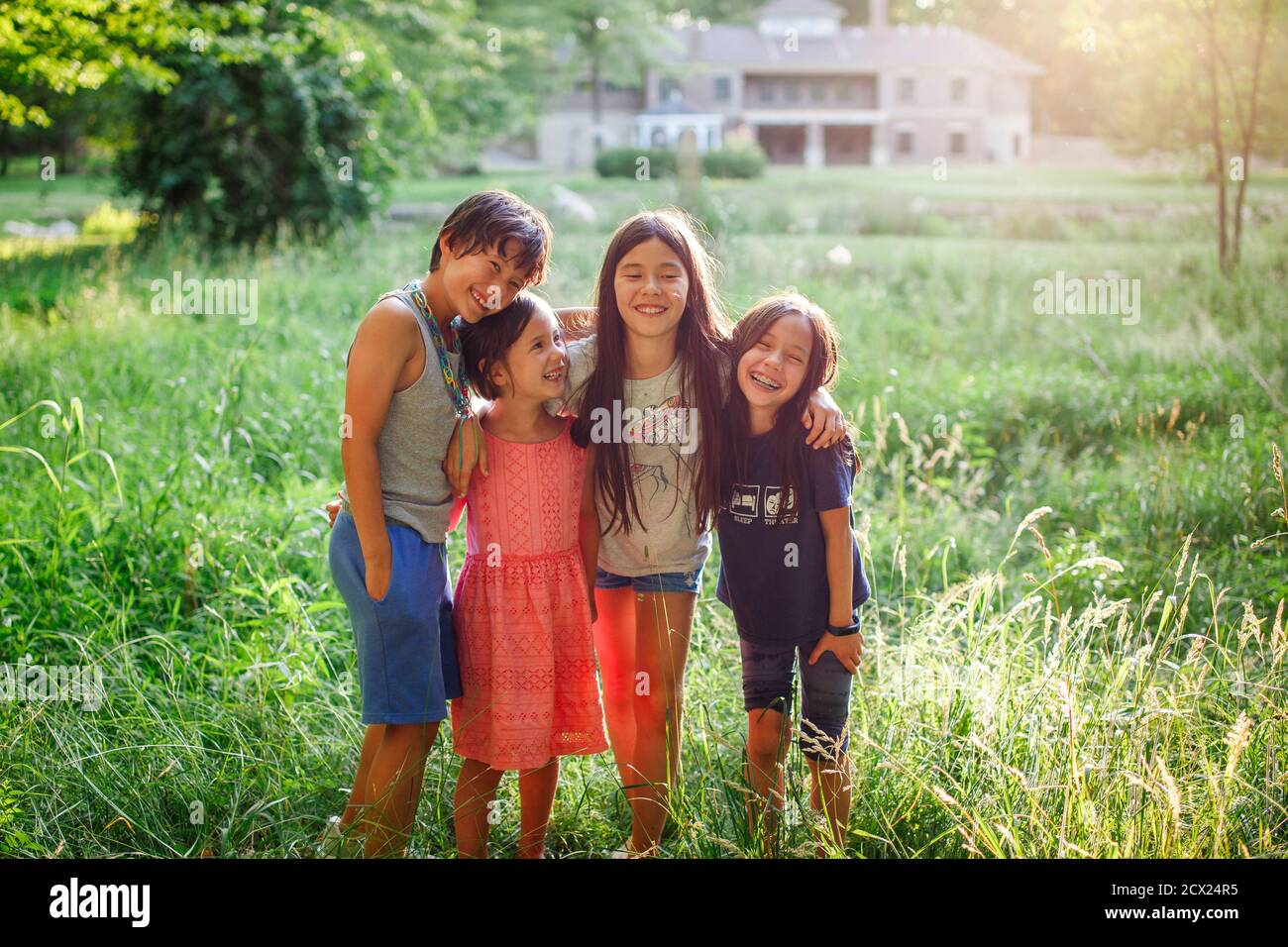 Happy children stand with arms around each other in sunlit field Stock