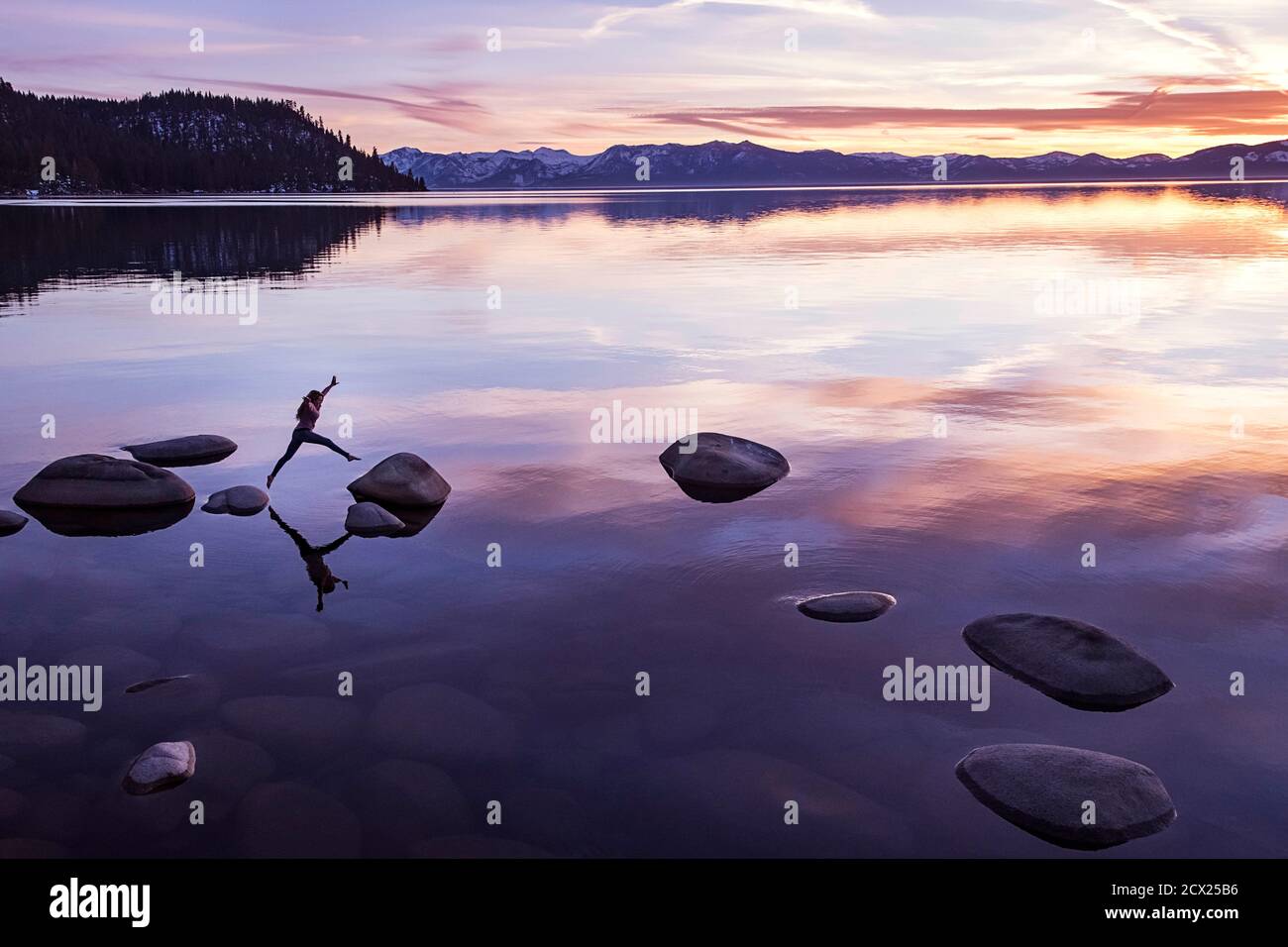 Carefree woman jumping on rock at Lake Tahoe during sunset Stock Photo