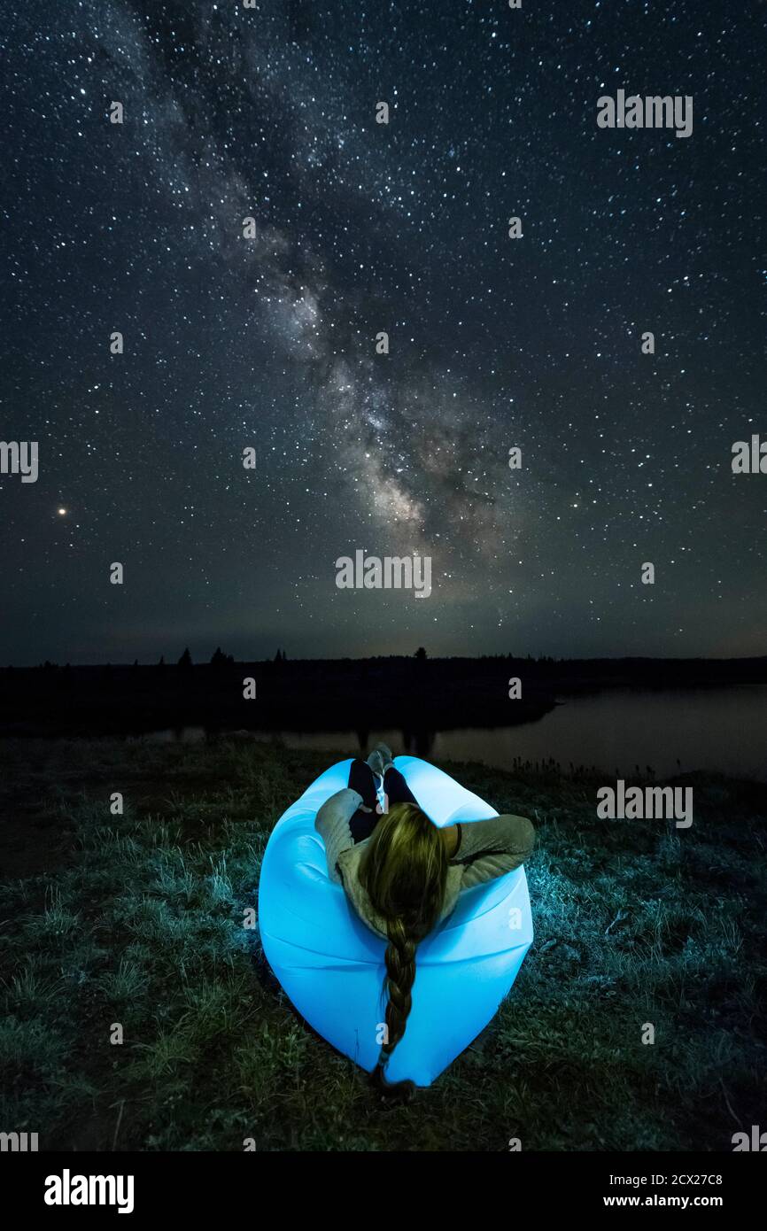 Woman relaxing on illuminated inflatable chair on field against star field Stock Photo