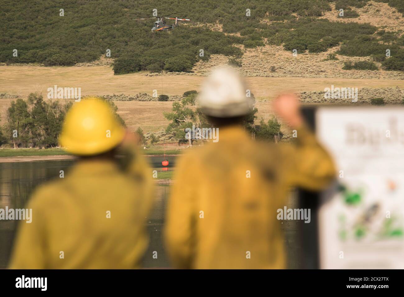 Rear view of firefighters looking at helicopter flying with fire retardant Stock Photo