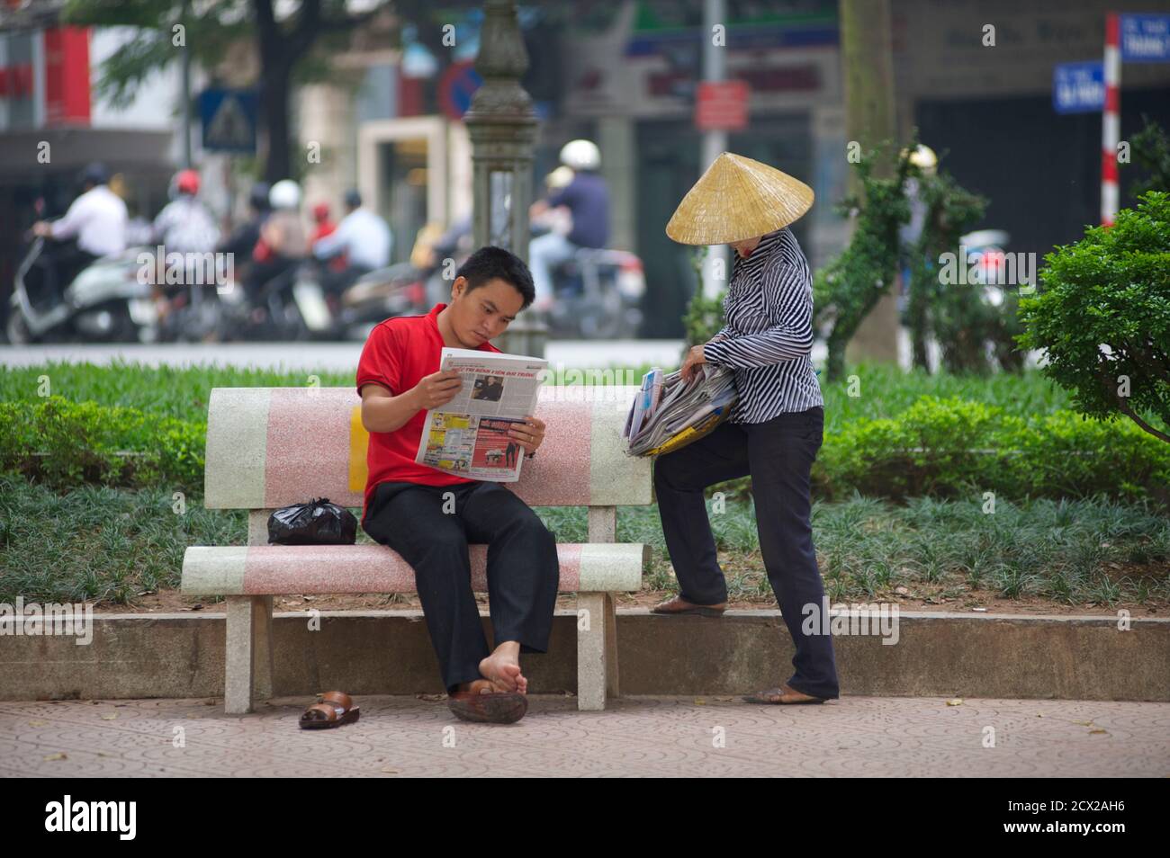 Newspaper vendor and man reading, alongside  Hoan Kiem Lake, Hanoi, Vietnam Stock Photo