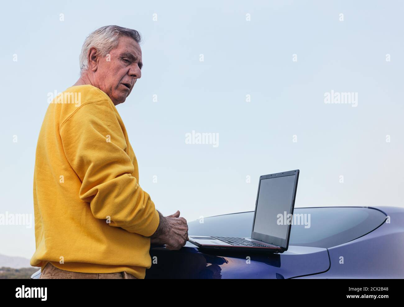 Senior man using laptop on car Stock Photo