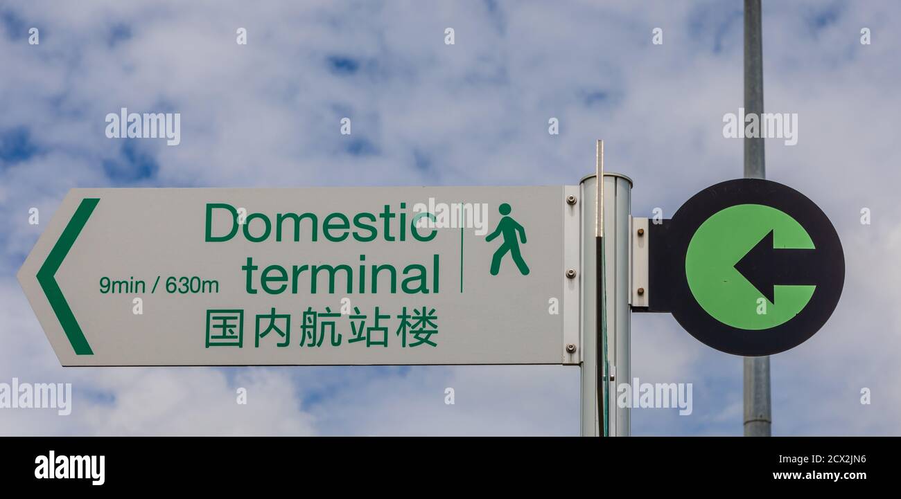 Bilingual direction sign 'Domestic Terminal' in English and Chinese at Auckland International Airport, marking the footpath between the two terminals. Stock Photo