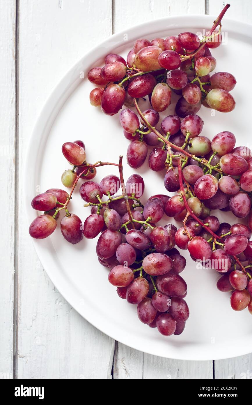 Ripe red grapes in a plate on a white wooden background. Top view. Stock Photo