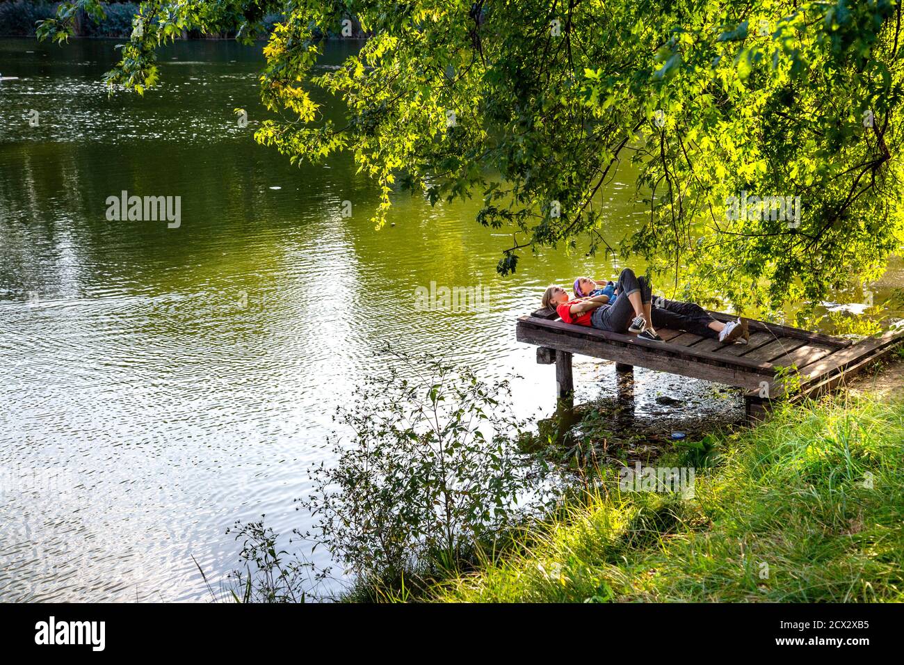 Two teenagers lying on a pier by a lake at Szczesliwicki Park (Park Szczęśliwicki), Ochota district, Warsaw, Poland Stock Photo
