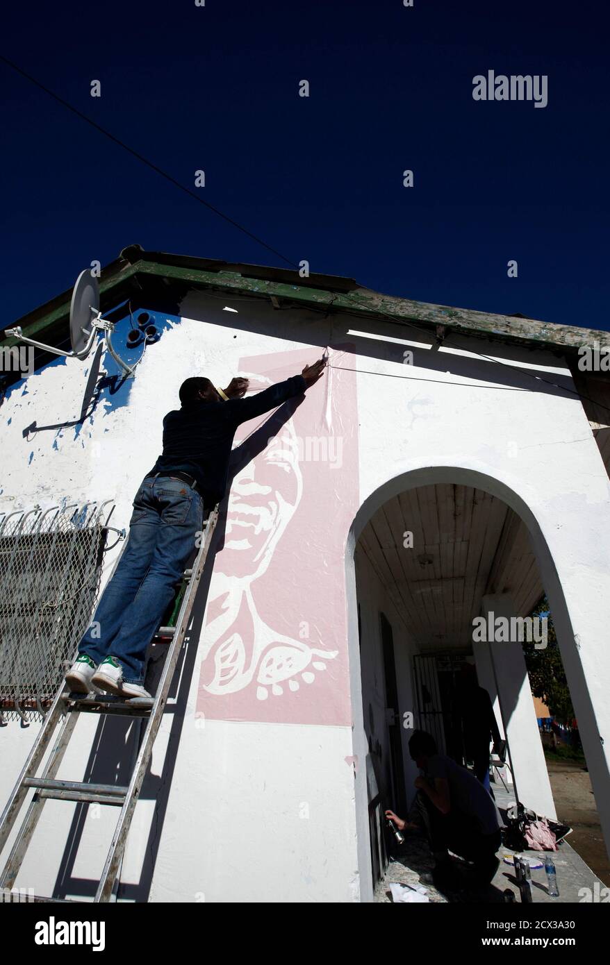 A volunteer paints a mural depicting the life of former President Nelson Mandela at a library in Cape Town's Imizamo yethu township, July 18, 2012. Thousands of South Africans heeded the call to offer 67 minutes of their time to help build communities as part of celebrations of Mandela's 94 birthday today. REUTERS/Mike Hutchings (SOUTH AFRICA - Tags: POLITICS ANNIVERSARY SOCIETY) Stock Photo