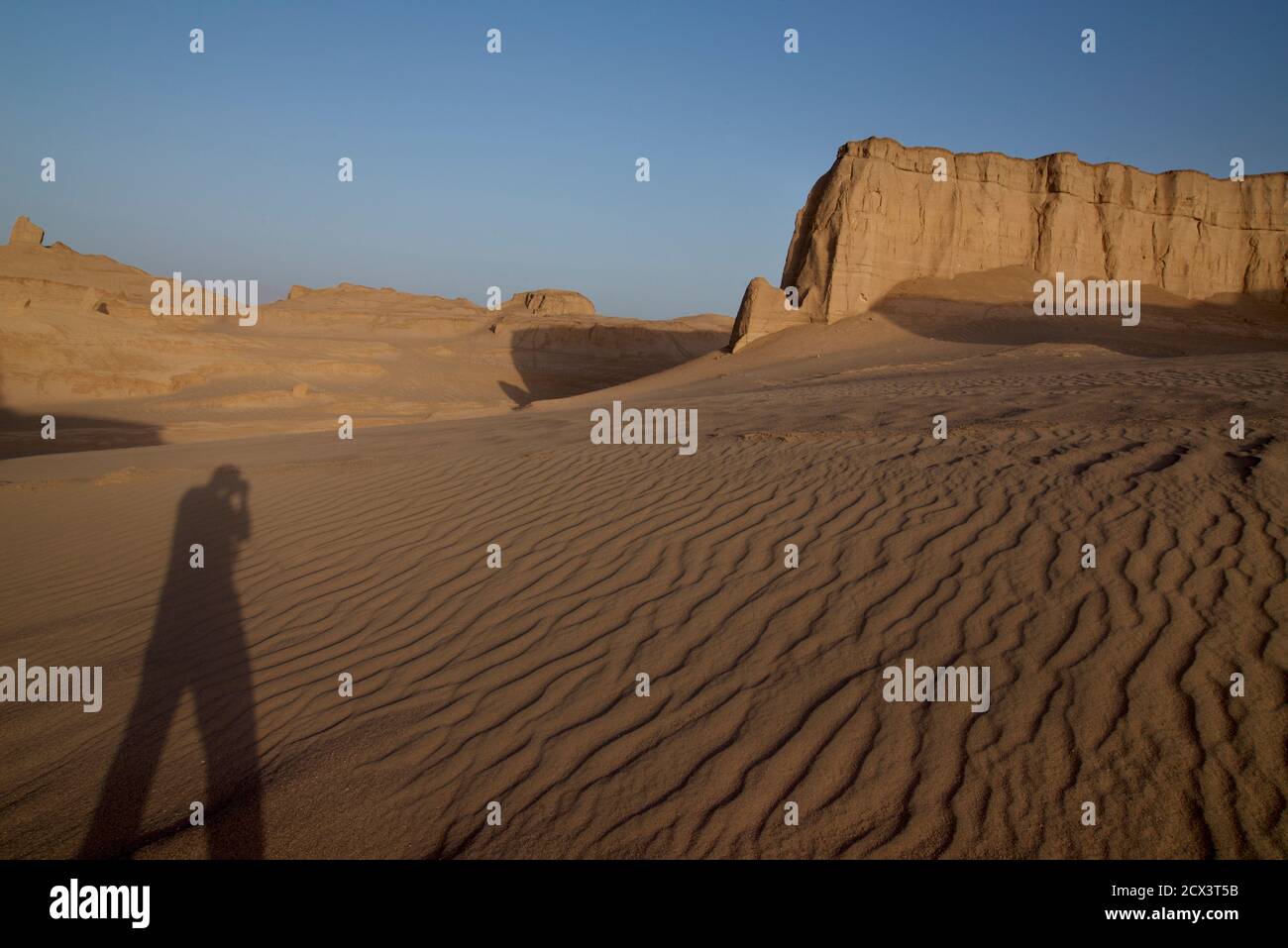 Long shadow of photographer taking photograph against desert backdrop. Lut desert, central Iran Stock Photo