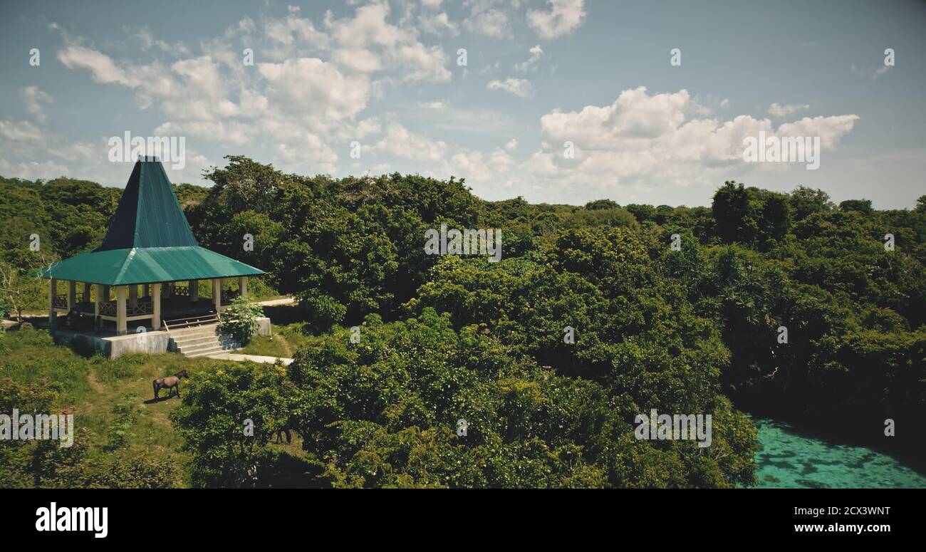 Indonesia landmark for tourists of modern building at green landscape. Architecture attraction at greenery grass, trees meadow with horse. Epic summer vacation at turquoise water of Weekurri Lake Stock Photo